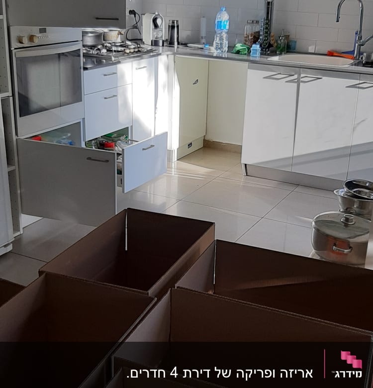 מטבח עם ארגזים פתוחים, מגירות פתוחות, בקבוק מים על השיש